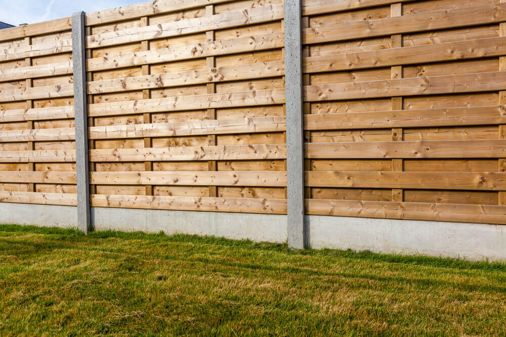 A large timber fence made of timber and steel support beams with grass infornt